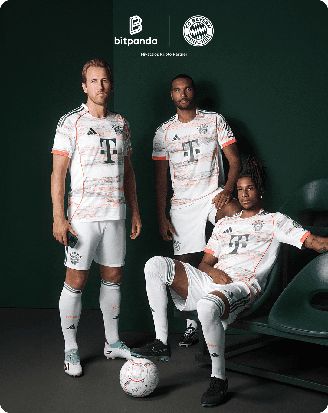 Three soccer players in white and orange jerseys pose indoors with a ball, showcasing the team's kit. Logos of Bitpanda and FC Bayern visible.